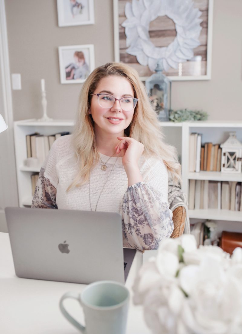 White woman wearing glasses in cream knit sweater in front of mac laptop