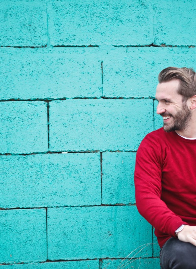 man wearing red sweatshirt and black pants leaning on the wall