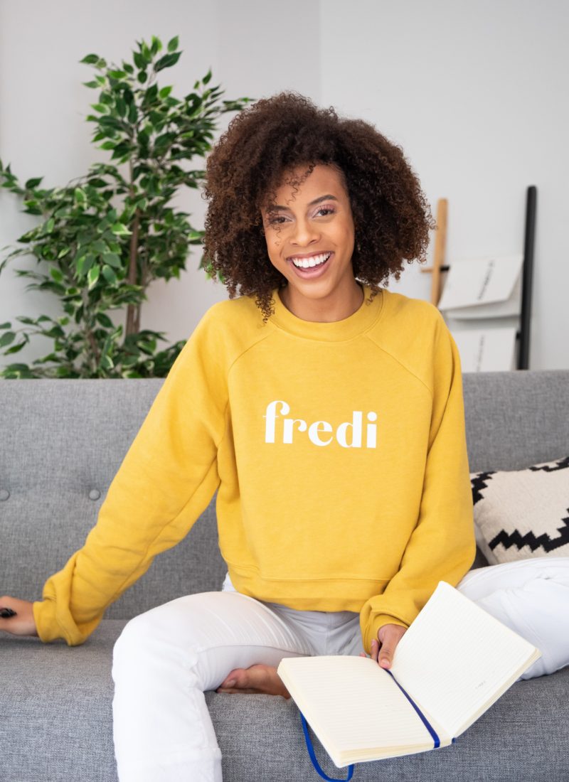 Mixed race woman with yellow sweatshirt smiling on couch raise vibration.