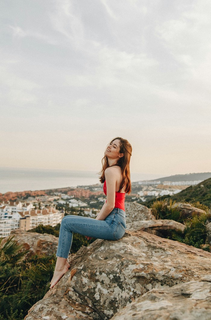 Girl on rock by the beach wearing red and jeans